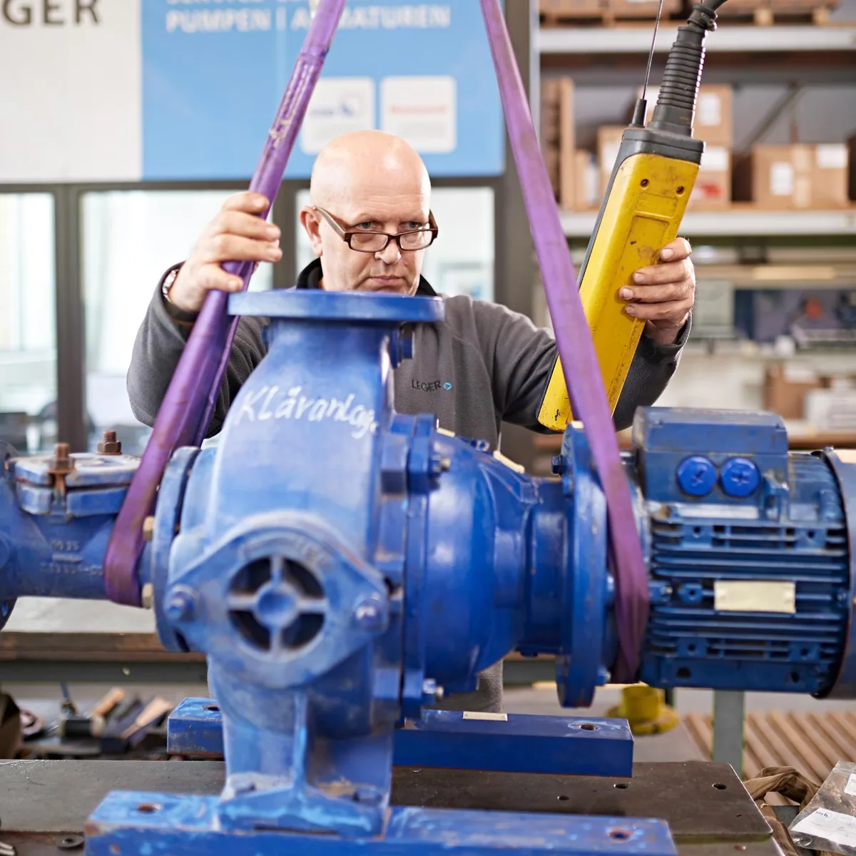 LEGER-Mitarbeiter hebt eine Normpumpe mit dem Kettenzug in der Werkstatt